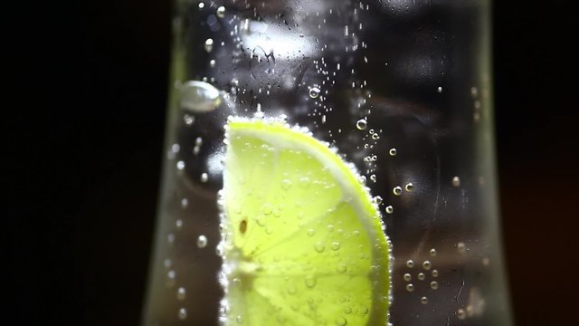 Color footage of a slice of lemon in a glass of soda, with ice cubes.