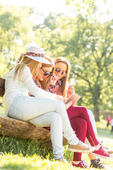 Group of three teenage girls sitting and chatting on bench in park.
