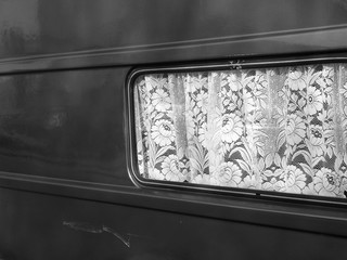 Gardine mit Rüschen im Fenster eines Wohnwagen für Vanlife und Camping bei Sonnenschein im...