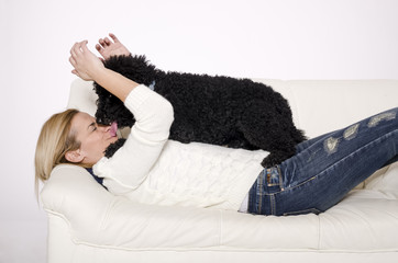 Woman lying on a white sofa with a black poodle.