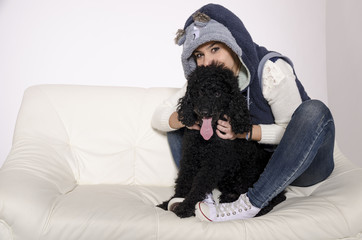 Woman with funny hood on a white sofa with a black poodle.