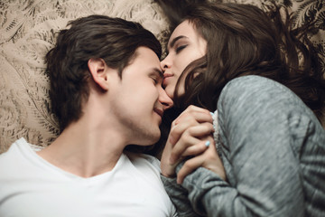 beautiful brunette girl and guy lying in bed and holding tightly hands. The concept of tenderness and affection