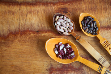 Carved wooden spoons with three sorts of beans on a textured wooden background with copyspace