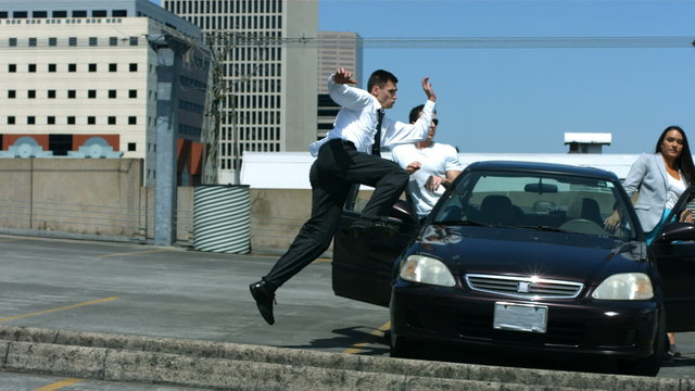 Business man runs through parking lot jumping over car