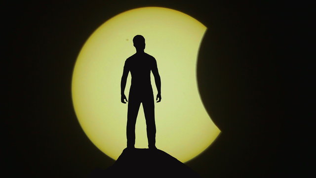 The man stand on a cliff on the background of solar eclipse. Real time capture