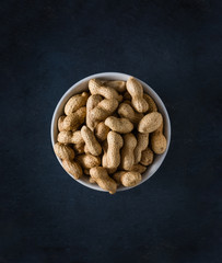 Bowl filled with organic peanuts. Top view with dark blue texture and empty space for text and other elements