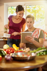 At kitchen. Nice couple cooking vegetables while using a tablet