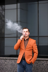 Young man smoking electronic cigarette on background of building