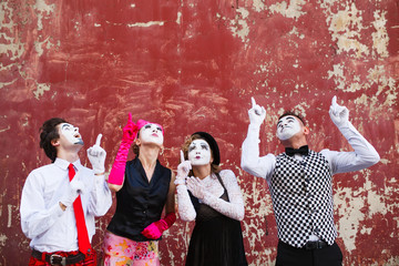 Four mimes point to the top on a red wall.
