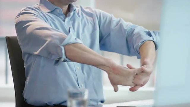 business man at office desk rolling up left sleeve, stretching fingers