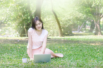 Woman sitting on grass field for playing computer in the park