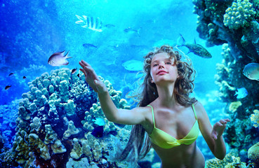 Girl is diving under water  amoung coral fish.