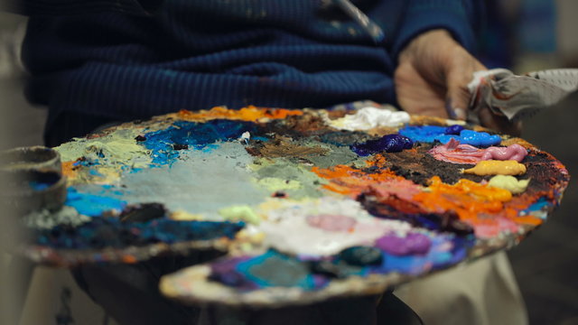 Artist mixes oil paints on pallet with various colors