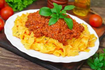 Traditional Italian pasta Bolognese or Bolognese with cooked pasta noodles topped with a spicy tomato based meat sauce garnished with fresh basil on a wooden background