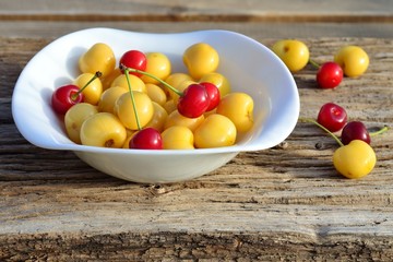 yellow and red cherries in white plate on old wooden Board