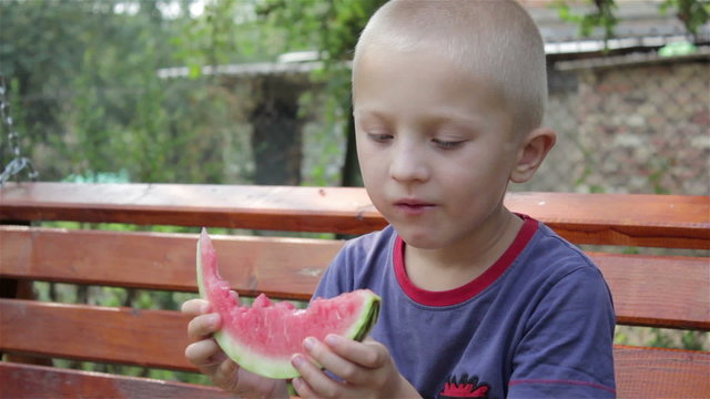 boy eating watermelon/summers  boy on a bench eating a watermelon red
