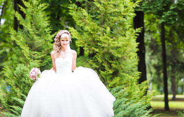 Fototapeta na wymiar Beautiful bride with wedding bouquet of flowers outdoors in green park.