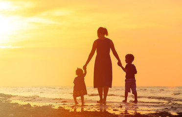 mother and two kids walking on beach at sunset