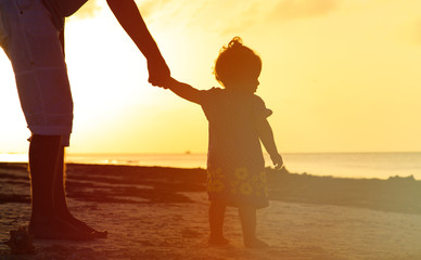 Fototapeta premium Silhouette of father and little daughter walking at sunset