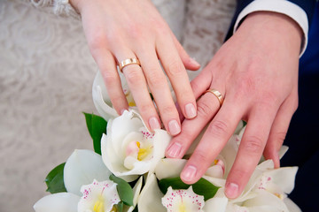 Bride and groom hands with engagement rings and wedding bouquet