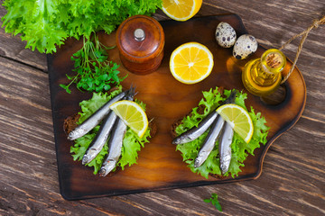 Traditional Spanish sandwiches with anchovies, lettuce and lemon on a wooden background