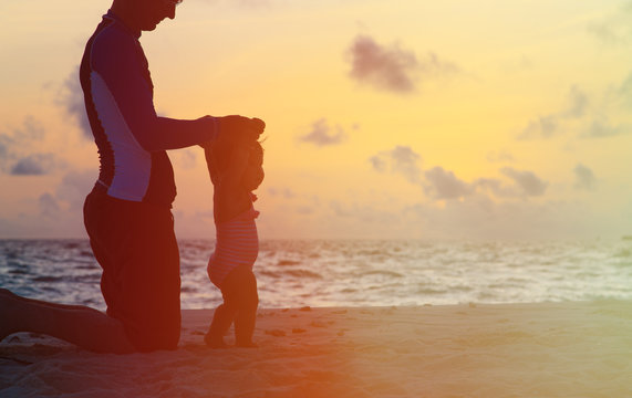 Silhouette of father and little daughter walking at sunset
