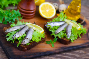 Traditional Spanish sandwiches with anchovies, lettuce and lemon on a wooden background