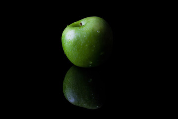 Green fresh ripe apple on black background with reflection from side