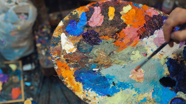 Artist mixes oil paints on pallet with various colors