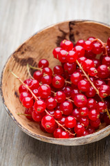 Redcurrant on a branch close to a wooden bowl.