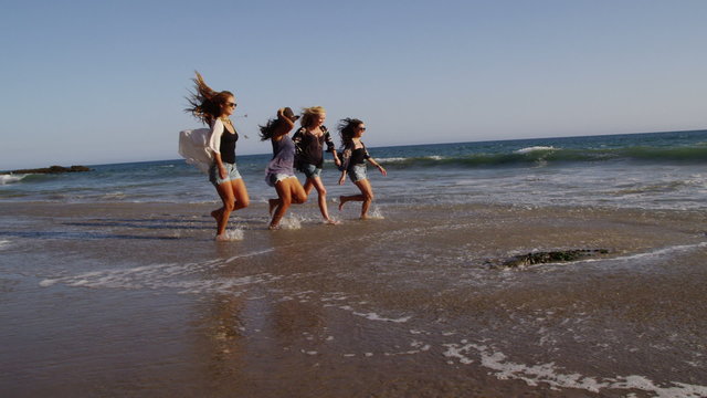 Group of young women at beach run in surf
