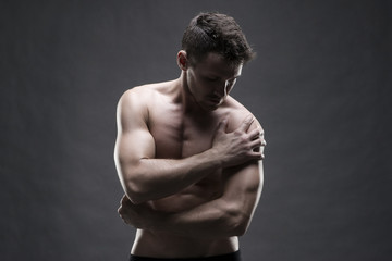 Fototapeta premium Pain in the shoulder. Muscular male body. Handsome bodybuilder posing on gray background. Low key close up studio shot