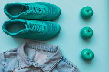 Flat lay fashion set : jean jacket, green sneakers and apples on light-blue pastel background