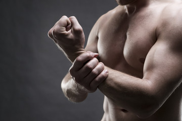 Pain in the hand. Muscular male body. Handsome bodybuilder posing on gray background. Low key close...