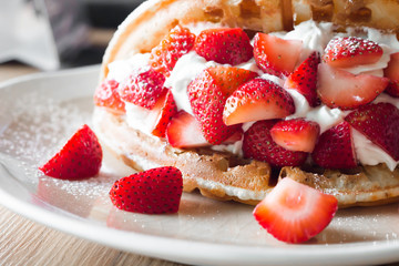 Strawberries waffles with vanilla ice cream on white plate.