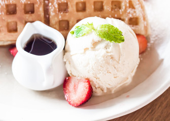 Strawberries waffles with vanilla ice cream on white plate.
