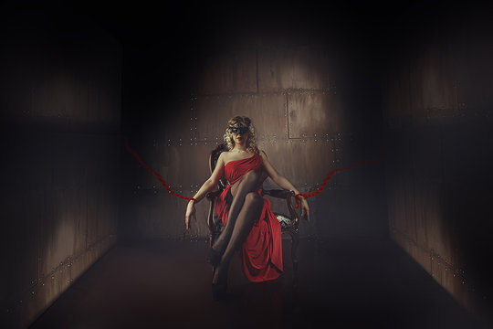 a woman in mask tied to a chair in an empty room