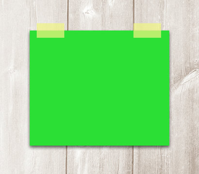 Hanging green paper note sign with empty space on white wooden background.