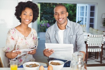 Smiling couple reading magazine and documents during breakfast