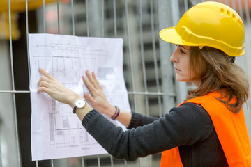 Profile portrait of female architect at construction site pointing office blueprints holding on scaffolding © cineberg