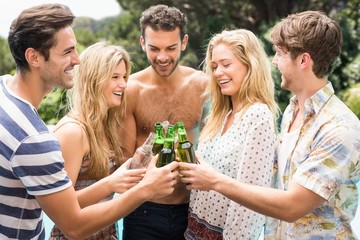 Group of friends toasting beer bottles near pool