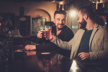 Cheerful old friends drinking draft beer at bar counter in pub.