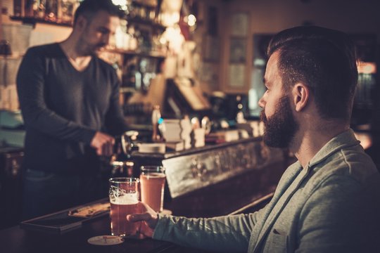 Stylish Man Sitting Alone At Bar Counter With A Pint Of Light Beer.