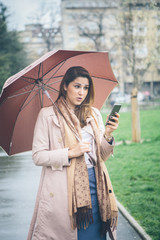 Young woman with umbrella at the park, using her mobile phone