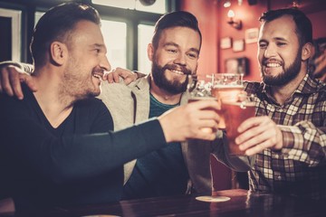 Cheerful old friends having fun and drinking draft beer in pub.
