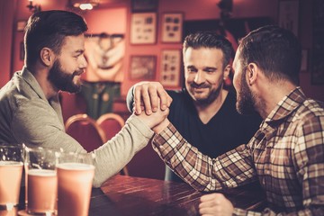 Cheerful old friends having fun arm wrestling each other in pub.