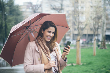 Young woman with umbrella at the park, using her mobile phone