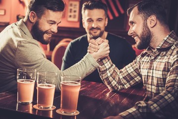 Cheerful old friends having fun arm wrestling each other in pub.