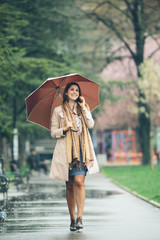 Young woman with umbrella at the park, talking on the phone