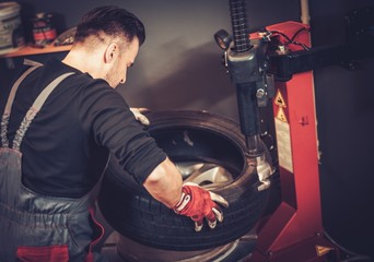 Fototapeta na wymiar Professional car mechanic replace tire on wheel in auto repair service.